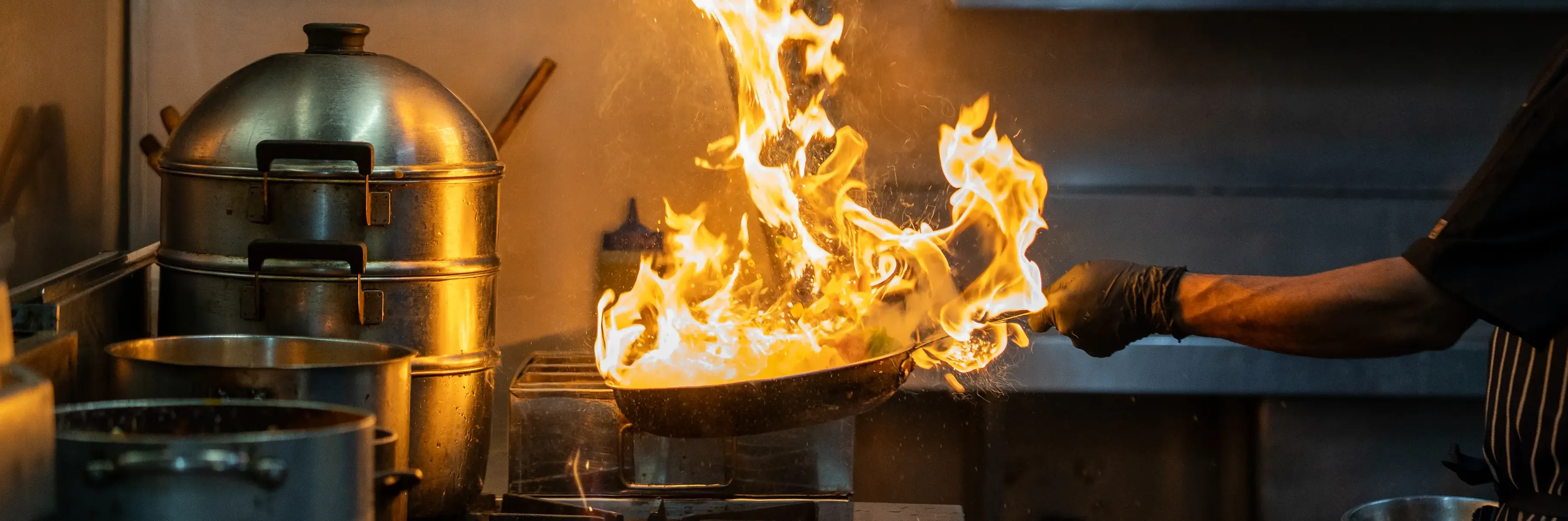 Chef tossing pan with high-reaching flames.
